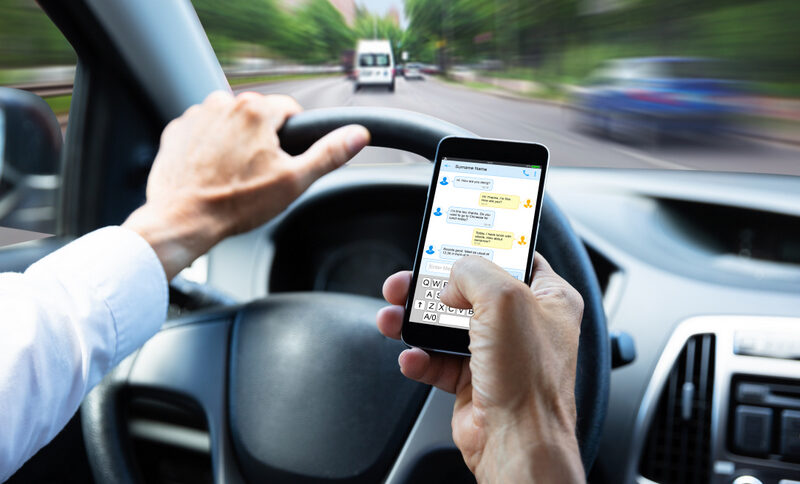 Close-up Of A Man's Hand Typing Text Message On Mobile Phone While Driving Car